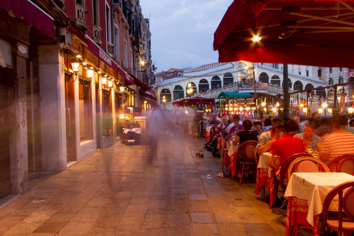 Outdoor dining served next to the Grand Canal, with *Ponte di Rialto* visible in the background.