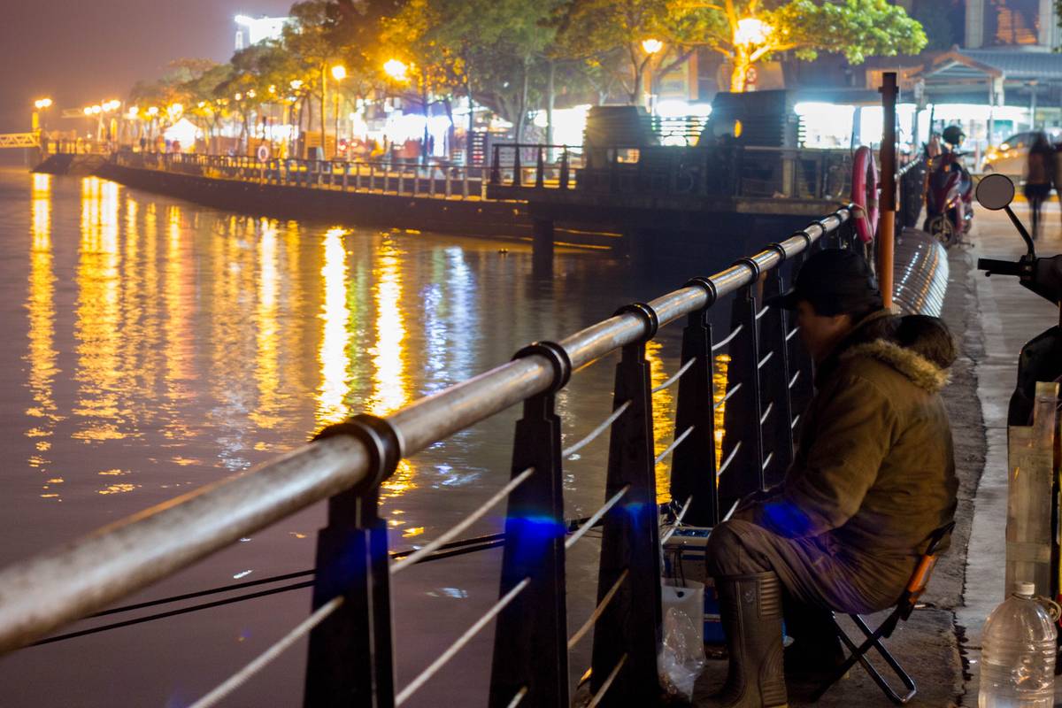 A man fishing at night at Tamsui District.
