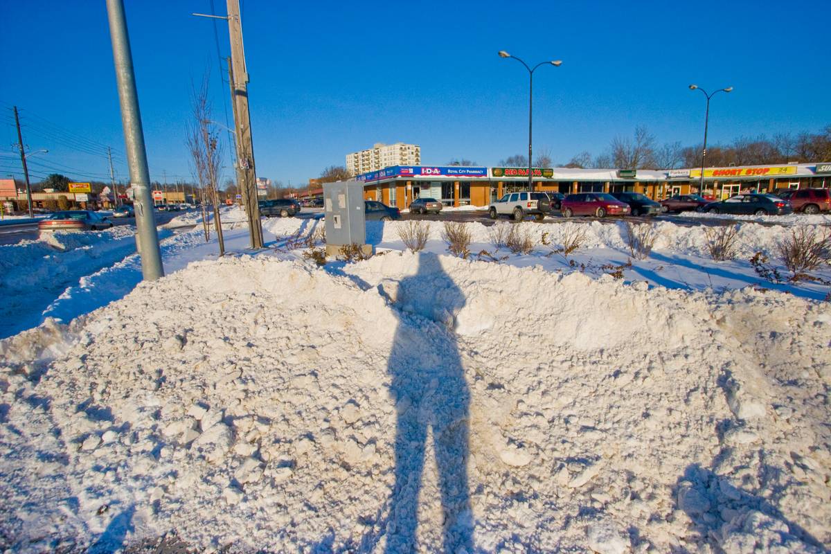 In the corner of Wellington and Gordon in Guelph, near sunset, with a long shadow of me taking picture of snow in front