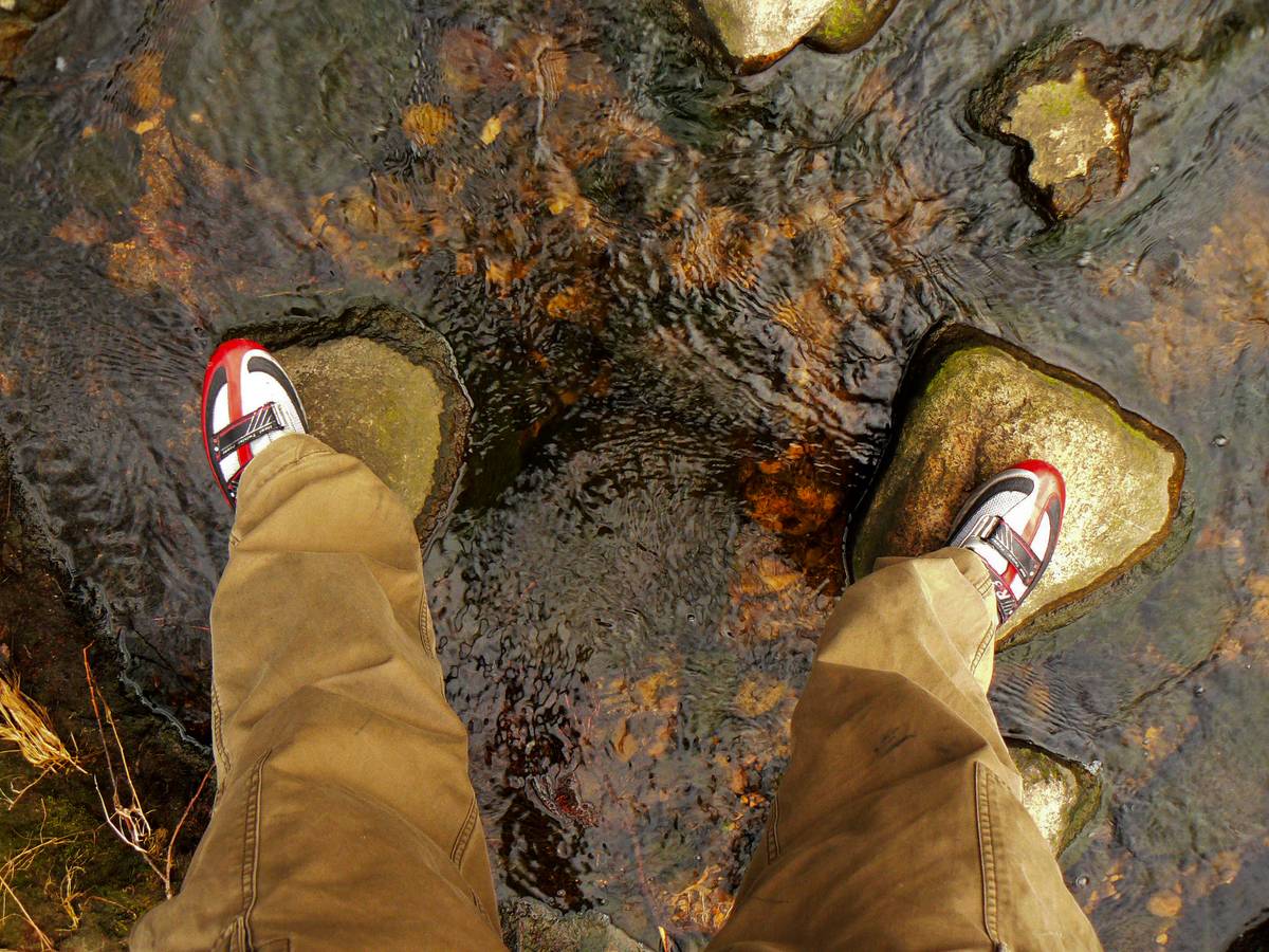 Looking down on a creek, with me standing on two rocks on my nylon-based shoes