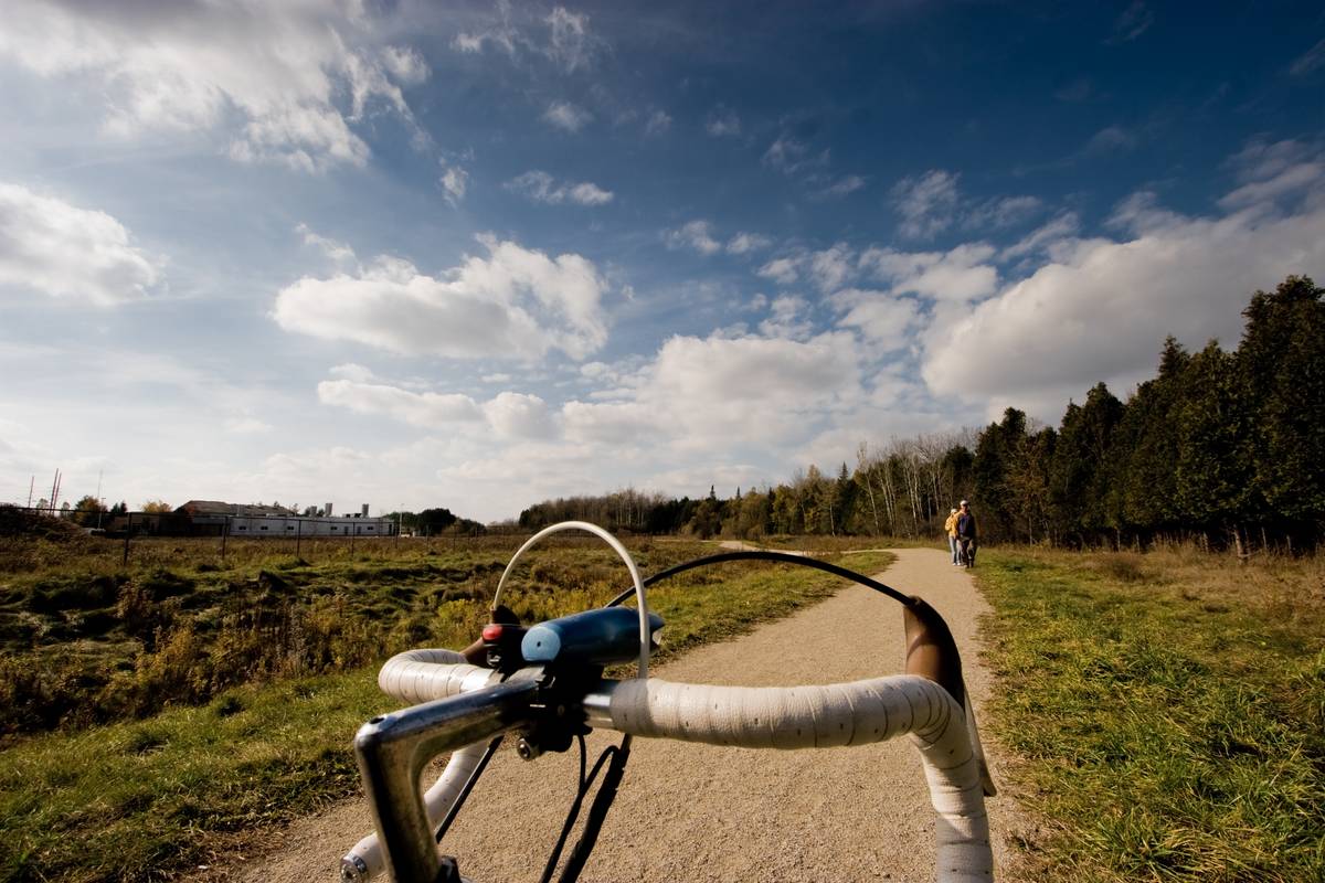 Looking up to the autumn sky with a wide view of the surroundings. White bicycle handlebars dominates the frame, a gravel trail leads the eyes out of the picture