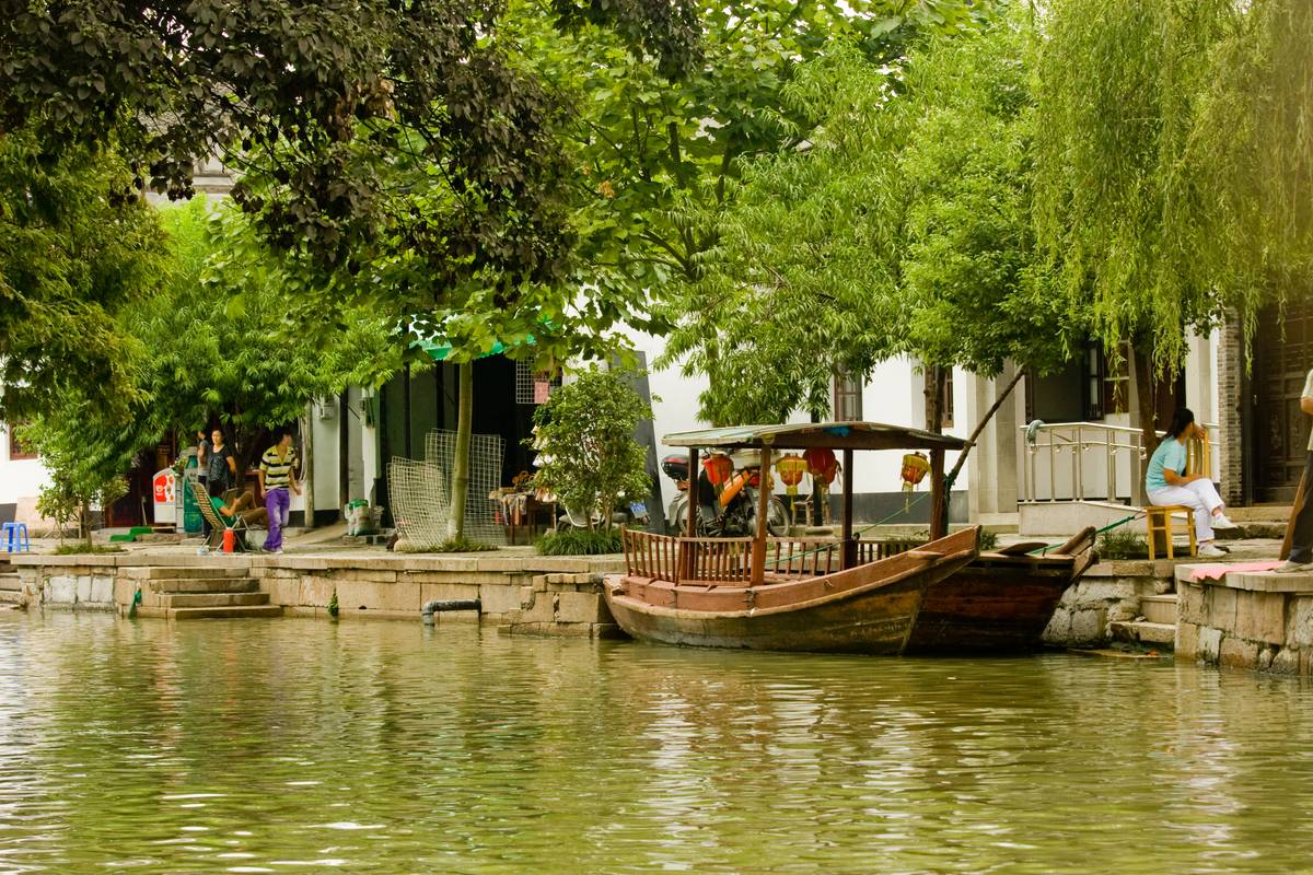 Willow trees line a riverbank, a boat rests anchored below