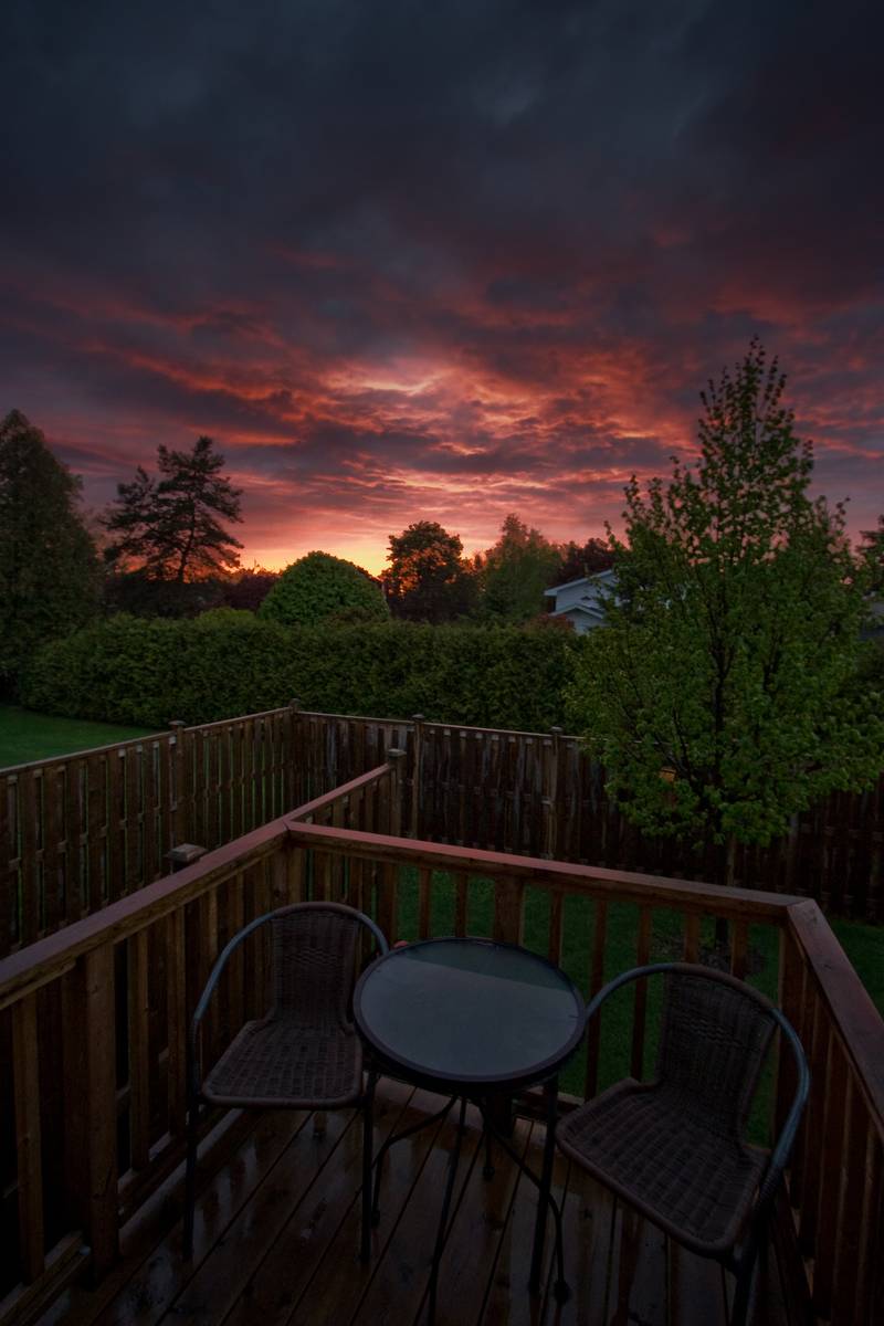 Two chairs astride a small table, on a deck, in front of a sunset